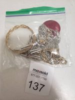 Plastic bag containing mixed custom jewelry including gold-toned bracelet, silver-colored chains, key and heart pendants.