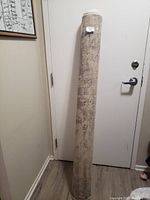 Rolled-up large beige and grey rug standing upright by a door, showing the full length rolled form.