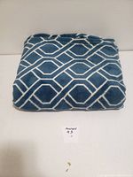 Folded plush blanket showing blue color with white geometric pattern.