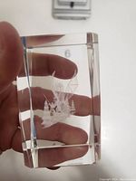 Hand holding rectangular crystal block showing etched dragon design inside.