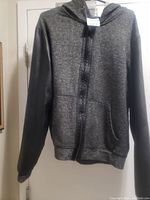 Front view of a medium size hooded jacket showing gray knitted fabric body and black leather sleeves, front zipper, and two front pockets.