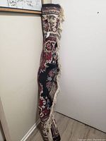 Photo of a rolled traditional patterned rug leaning against a wall, showing partial fringe and design details.