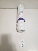 Photo shows rolled up white bath tub mat with textured suction cups on surface in original label packaging, placed on white surface with lot number card.