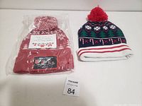Two Christmas knit hats displayed on a white background, one new in plastic packaging and one used with candy cane and tree patterns.