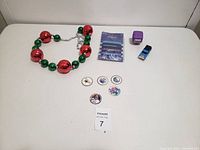 Image showing the red and green Christmas bead necklace, five NHL pogs, a purple plush head toy, blue toy truck, and a pack of bracelets.