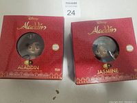 Front view of boxed Disney Aladdin and Jasmine figures showing characters' faces through round window plastic.