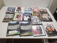 Top down image of 15 DVDs arranged on a white surface. Titles visible include war films, geological journey documentaries, comedies like Pink Panther, and the Godfather series.