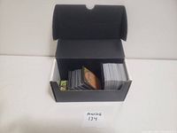 Black storage box open showing a large number of Magic: The Gathering cards stored upright inside. The cards appear in excellent condition with some sleeved and others loose.