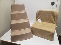 Photo showing two pet staircases side by side: a beige plastic one with four steps and a smaller, beige fabric-covered two-step staircase.