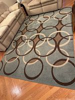Full view of the area rug laid beneath couches on hardwood floor showing the blue base with brown, taupe, and off-white circular pattern.