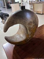 Front and side view of an artistic crescent-shaped clay vase with small neck and opening, showing earthy distressed pattern.