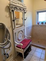 Full view of the white painted coat bench with red cushion seat, tall mirrored back with hooks, and drawer underneath.