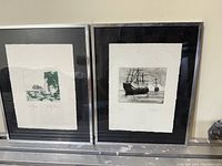 Photo of two framed lithographs - on the left the still life in green ink, on the right the boat sailing scene in black and white.