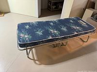 Folded twin mattress laid out on the floor supported by a metal bed frame, showing floral mattress on top and sturdy frame base.