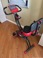 Side angle showing folding exercise bike with digital console, padded seat, and pedals.