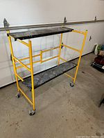 Open scaffold showing two black platforms and four caster wheels in garage setting