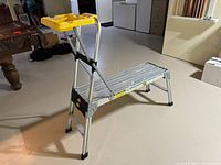 Photo of an aluminum folding work platform in used condition showing structure, yellow tool tray, and platform surface
