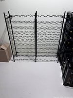 Full view of black metal wine rack showing horizontal wavy bottle supports and vertical side supports.