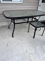 Large rectangular tempered glass outdoor table with black metal frame and curved legs on a concrete patio