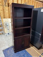 Full view of one dark wood bookcase showing two lower cabinet doors and three open shelves above.