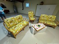 Photo of the entire rattan furniture set showing two two-seater sofas and one swivel chair with floral patterned cushions in a light-colored room.