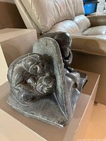 Side view of soapstone sculpture showing man crouched and bear figure, curved stone element behind them.