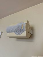Beige Mirage speaker mounted on wall with metal grille and label visible