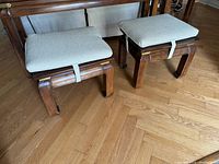 Pair of wooden stools with removable beige cushions on hardwood floor.