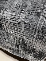 Close-up photo of rolled upholstery fabric showing texture and abstract linear pattern in black, white, and gray.