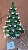 Full view of the ceramic Christmas tree showing green textured branches, white snow accents, colored bulbs, white base, and power cord with switch.