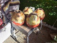 Four ceramic fire pots arranged on a small metal table outside with a blanket-covered chair partially visible.