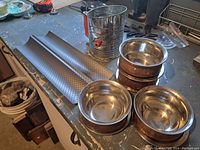 Photo showing all items on a countertop: two baguette loaf pans, a flour sifter, and the four copper bowls grouped together.