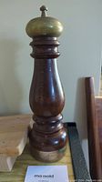 Front view of a tall wooden pepper mill grinder with brass top and base, showing its turned wood body design.
