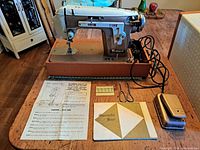 Full view of Piedmont sewing machine with power cord, instruction manual, needles, metal accessory case, and cover on the table.