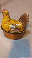 Yellow brown ceramic hen-shaped casserole dish with lid showing textured feather details.