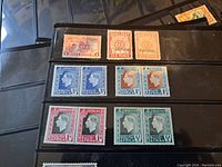 Close-up photo of black protective stamp album page with various South Africa stamps featuring Queen Elizabeth and King George VI, including multiple denominations in blue, red, orange, and green.