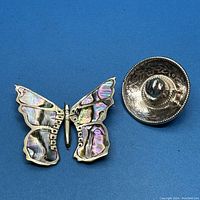 Butterfly and sombrero sterling silver brooches side by side on blue background showing details and condition