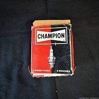 Outer box of Champion spark plugs, showing brand logo and quantity (8 spark plugs). Box is worn and opened.