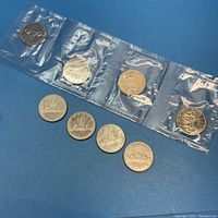 Four 1969 Canadian nickel dollars sealed in original plastic packaging along with four 1972 loose coins laid on blue surface