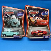 Front view of two sealed Disney PIXAR Cars collector cars, Mater and Lightning McQueen, in original packaging.