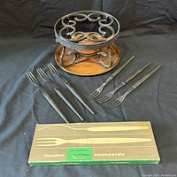 Set includes 8 fondue forks, small black iron trivet, and round copper tray with box for the forks in front.