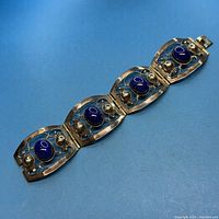 Full view of the bracelet stretched out, showing all five linked panels with blue stones and silver accents.