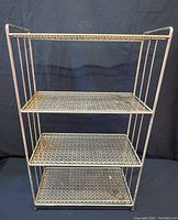 Front view of the vintage metal shelf showing four perforated shelves and tubular metal frame with some surface rust and wear.