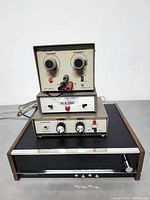 Four vintage Heathkit stereo components stacked: power supply on top with voltage and current knobs and red power LED, silver solid-state stereo pre-amplifier with power and input toggle switches in the middle, and Heathkit stereo amplifier with headphone jack, volume and tone knobs, and power switch at bottom. Behind is the Heathkit tuner model AJ-1214 with black front panel and tuning knob.