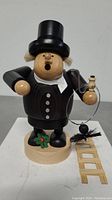 Front view of the wooden chimney sweeper figure showing the open mouth hole for incense, the black top hat, coat, and the chimney brush held in right hand.