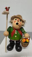 Front view of the Christian Ulbricht wooden farmer figurine showing green coat, red scarf, basket with fruit, and staff with red bird.