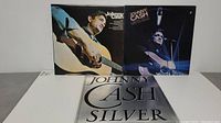 Three Johnny Cash vinyl LP records displayed: "Johnny Cash" self-titled album, "Silver" album, and a third album with Johnny Cash performing live on stage cover.
