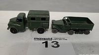 Two green Lesney toy vehicles side by side on a surface with lot label: radio truck with boxy cabin and personnel carrier with open truck bed, rubber wheels missing on one
