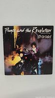 Front cover of Prince and the Revolution Lets Go Crazy 12-inch vinyl maxi single, showing Prince on a motorcycle under streetlights.