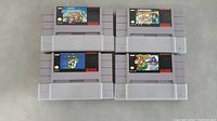 Front view of four SNES cartridges showing labels for Super Mario World, Super Mario All-Stars, Yoshi's Island, and Super Mario Kart.